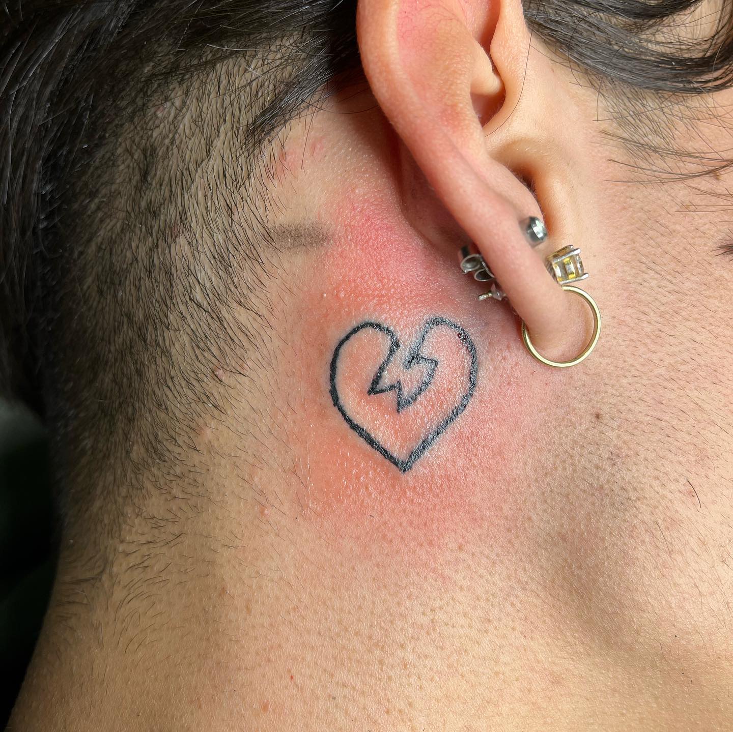 Tatuaje de corazón roto detrás de la oreja.