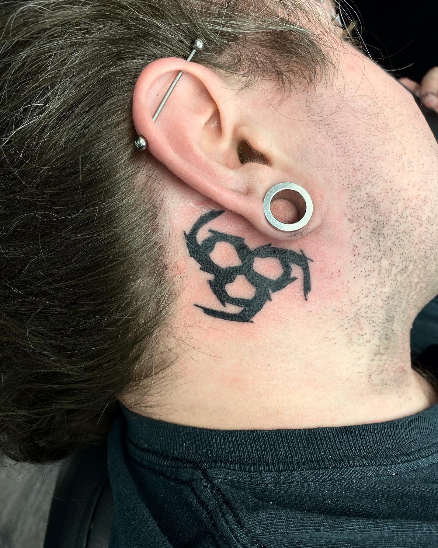 Tatuaje de tinta negra detrás de la oreja