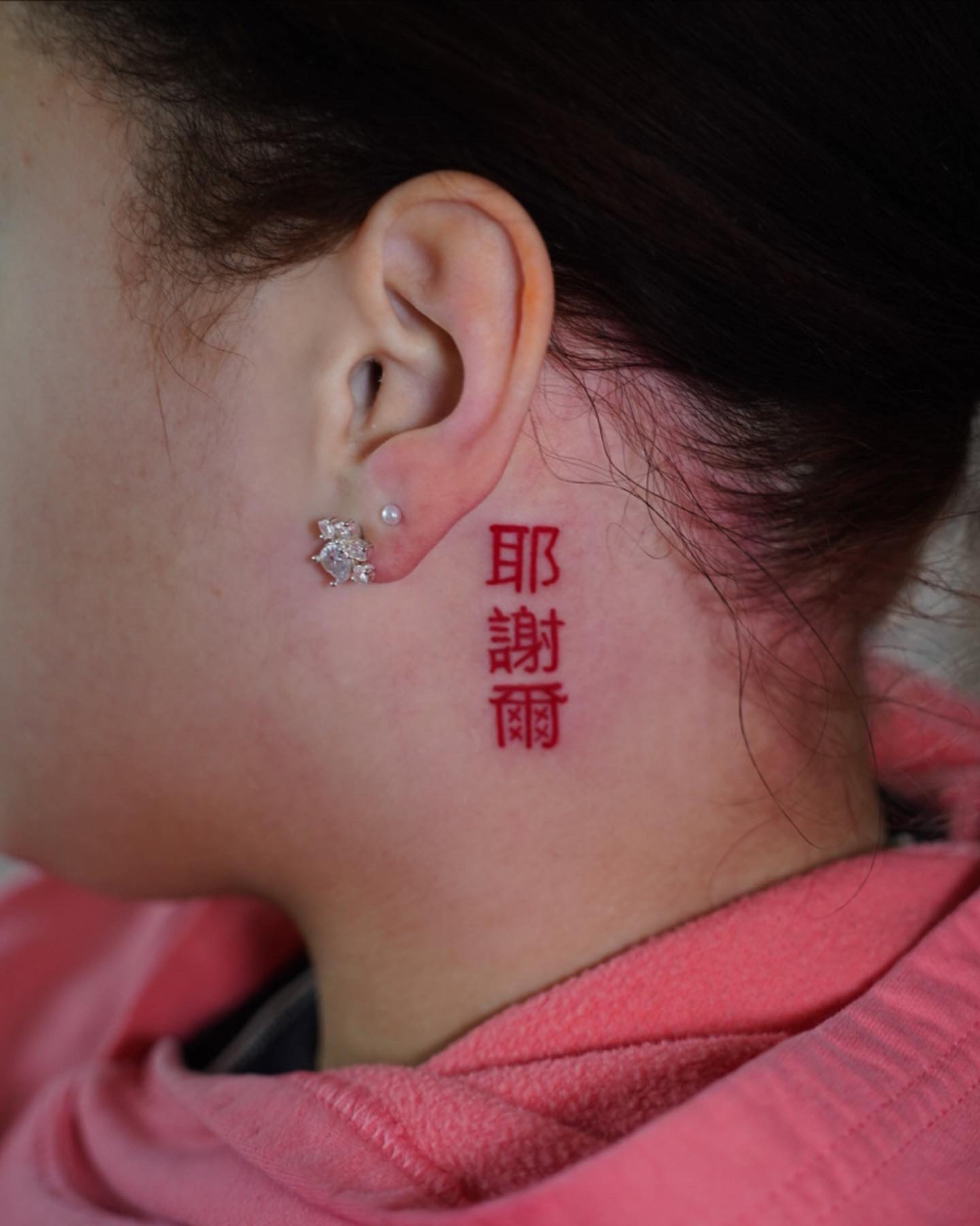 Tatuaje detrás de la oreja con letra china.
