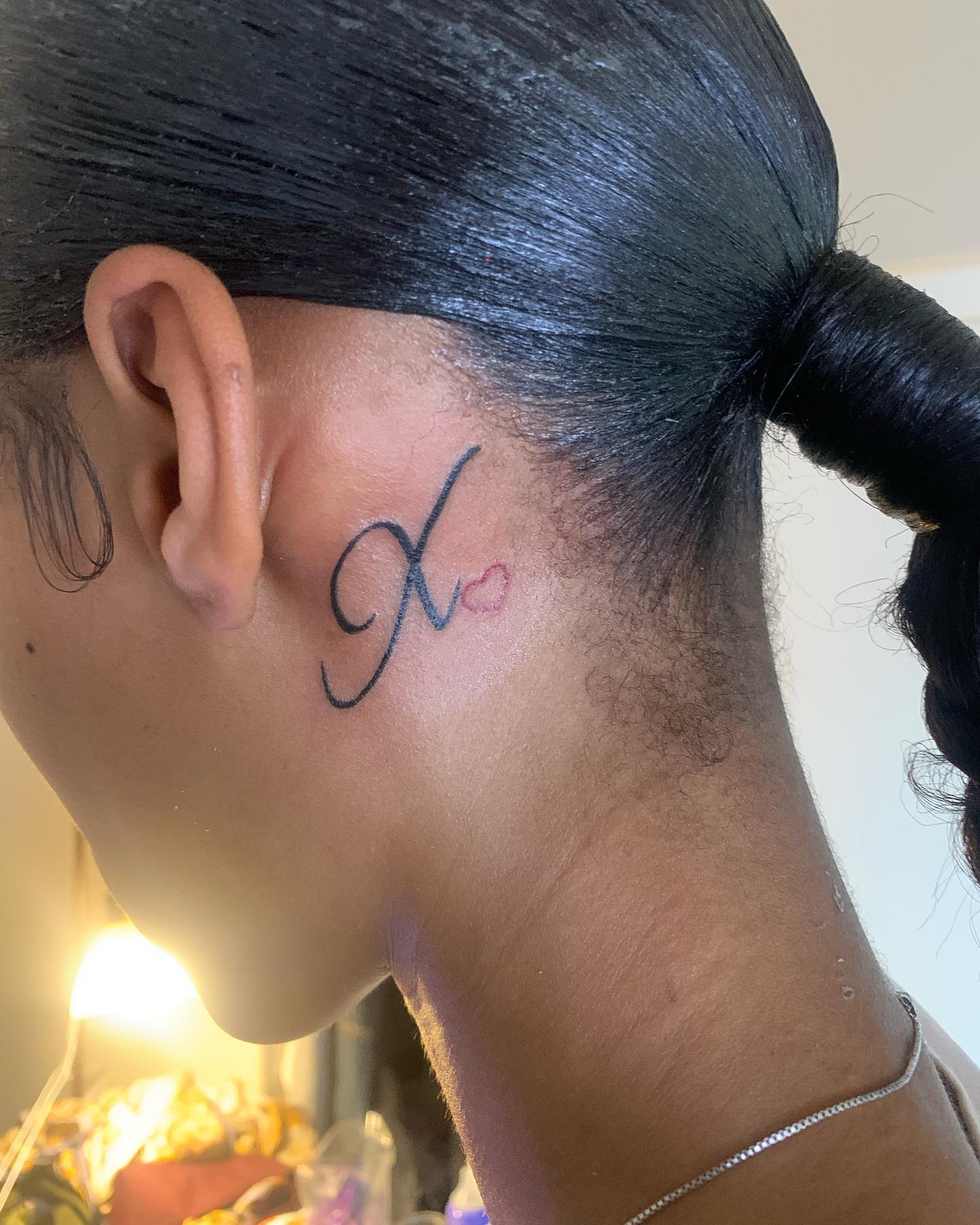 Tatuaje detrás de la oreja inspirado en una letra.