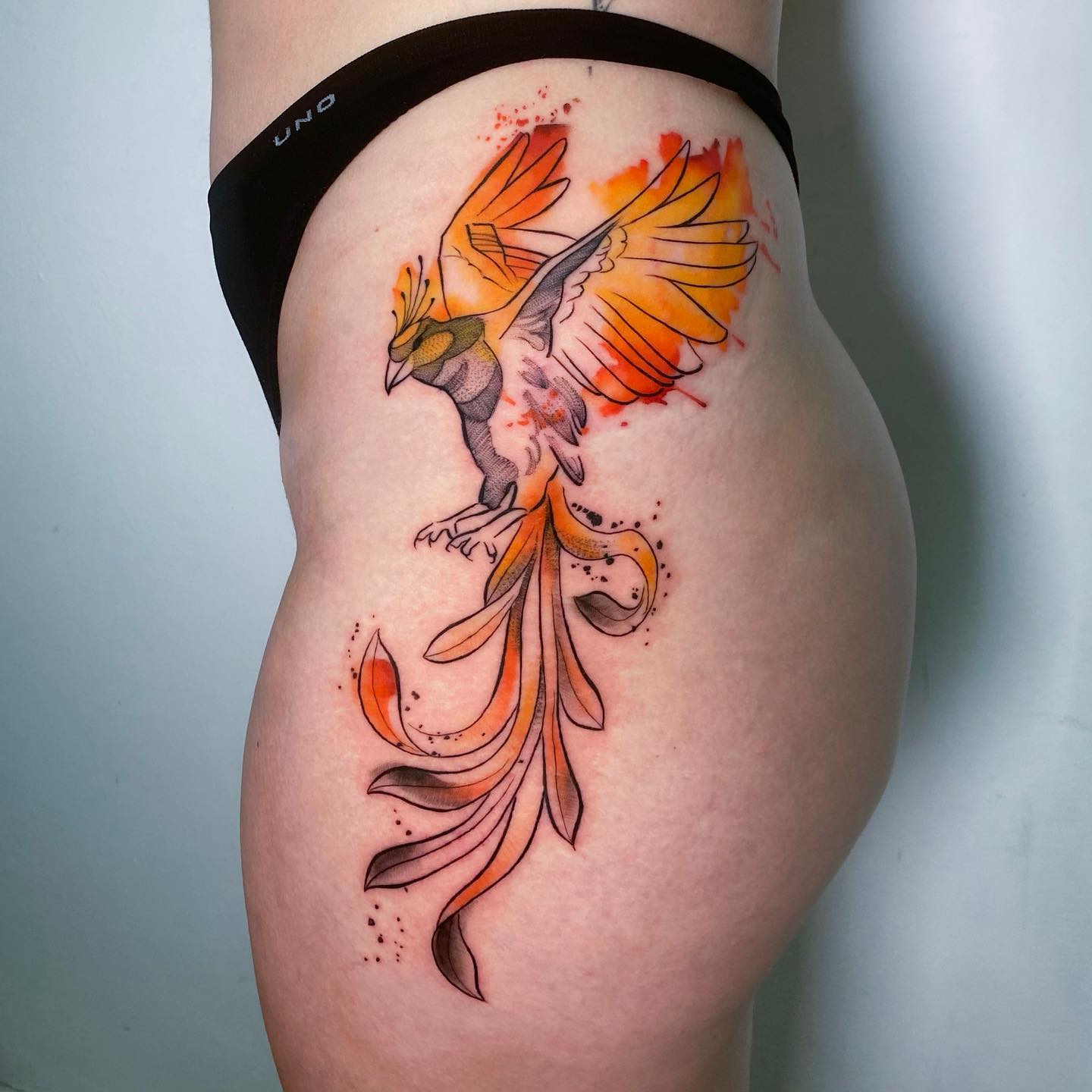 Fénix naranja tatuado en la cadera