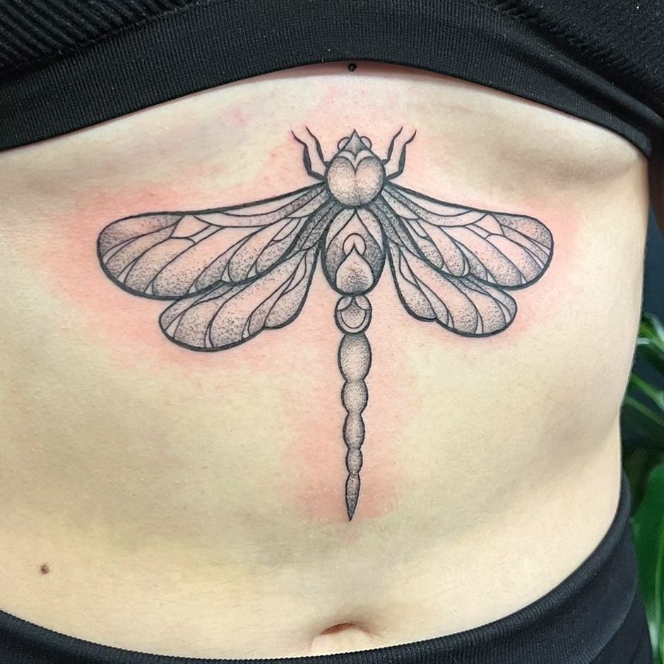 Tatuaje de libélula negra en el estómago.