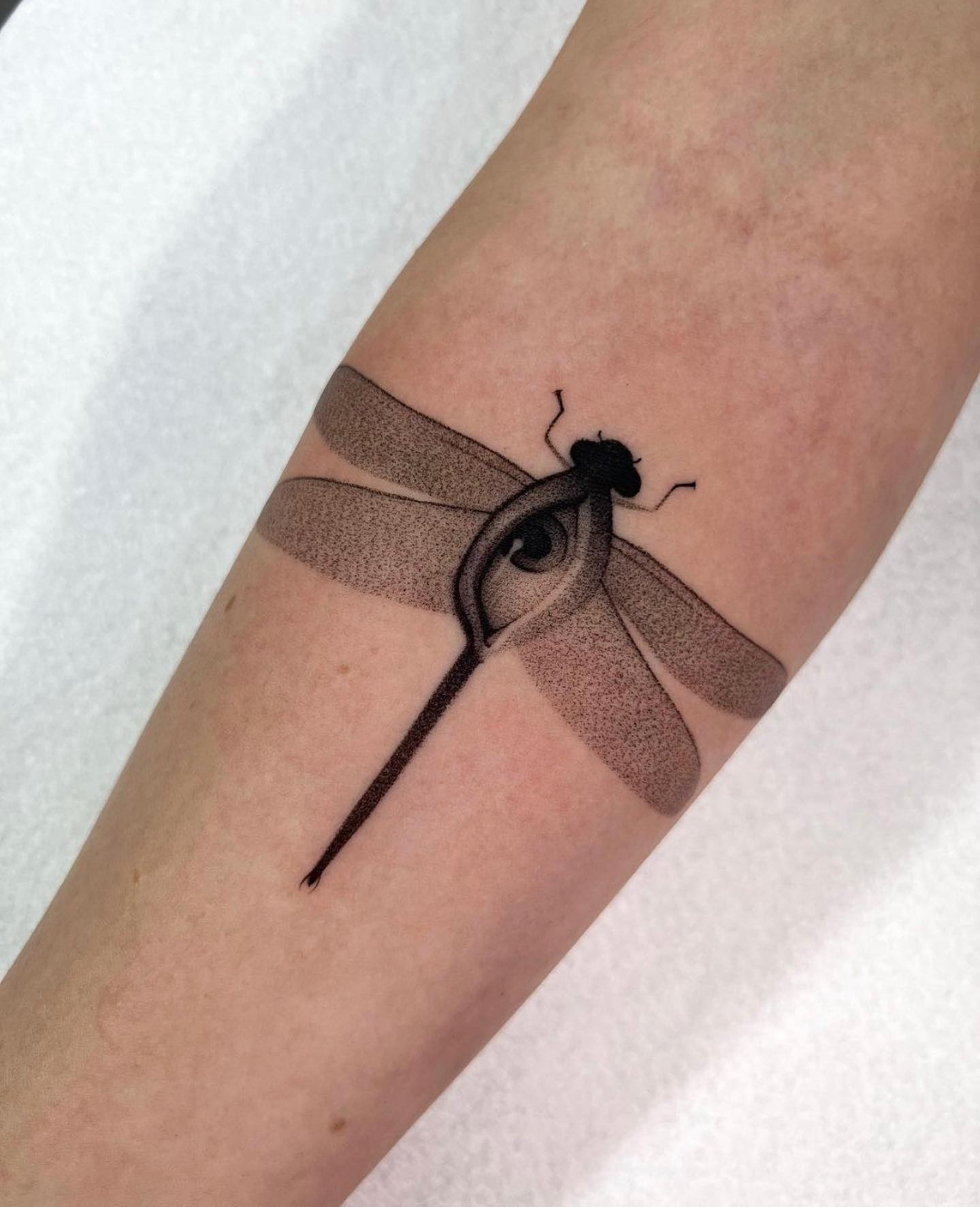 Tatuaje de libélula pequeña y negra.