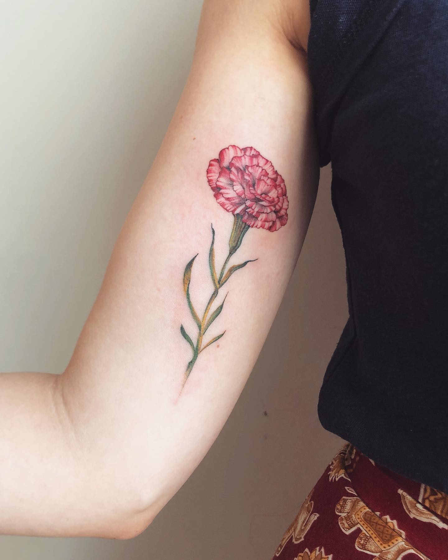 Tatuaje de flor clavel en el interior del bíceps.