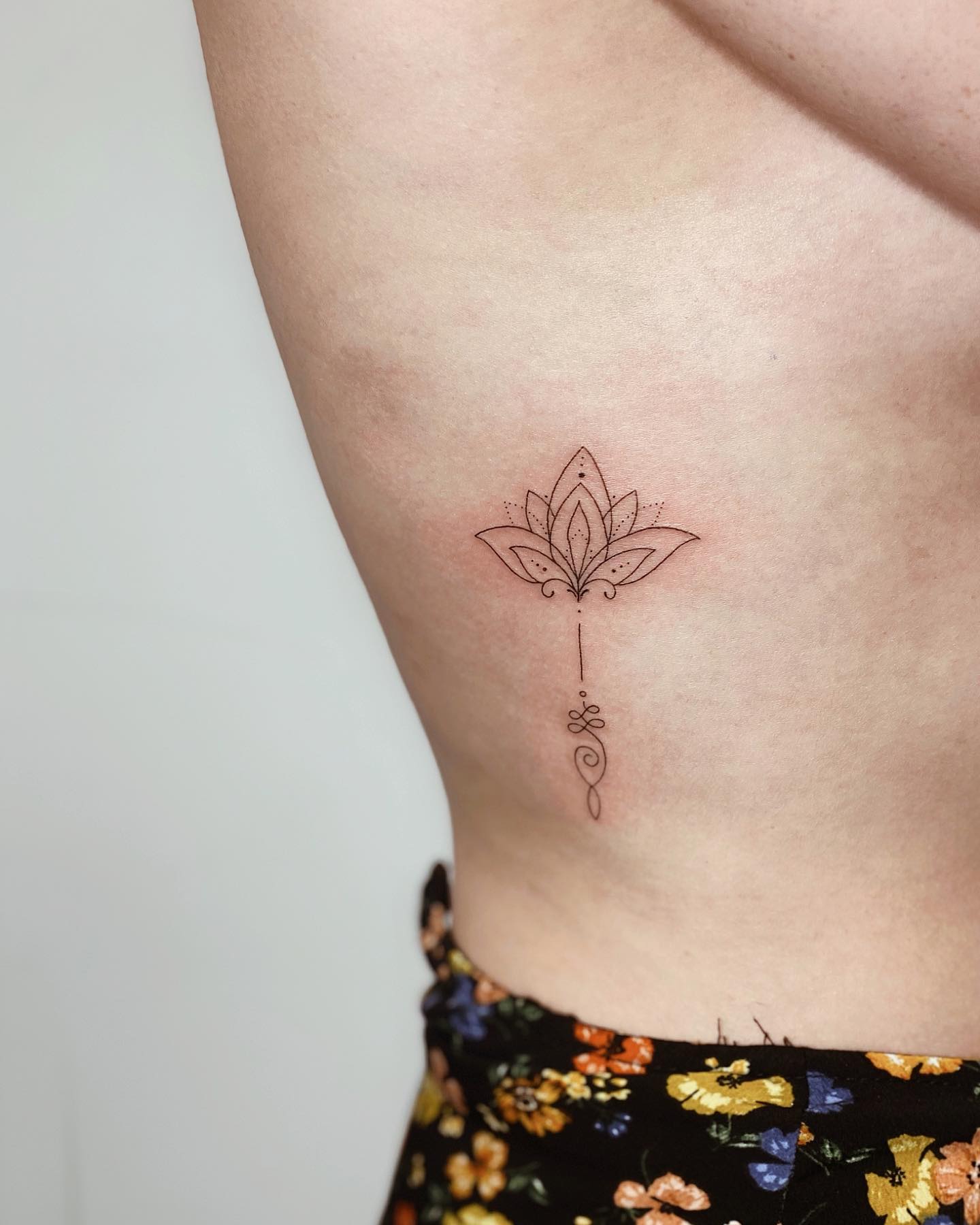 Tatuaje de línea fina y símbolo Unalome en la costilla lateral