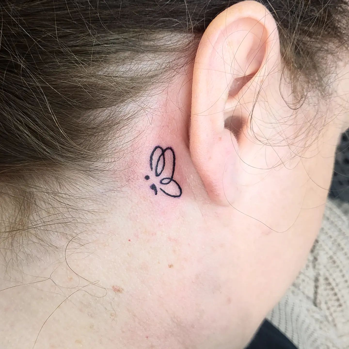 Tatuaje de punto y coma sobre la oreja.
