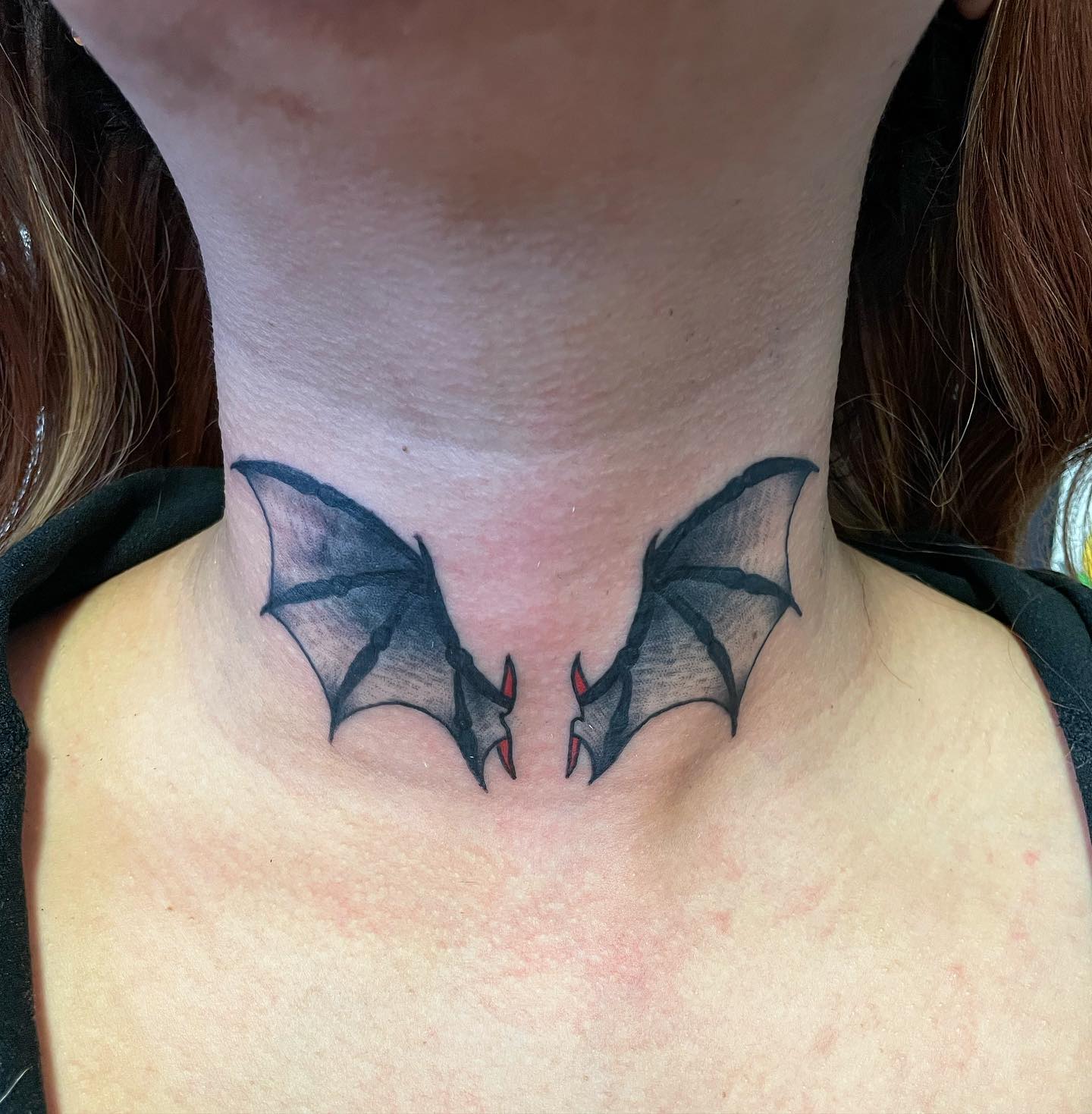 Tatuaje de alas de murciélago en el cuello.