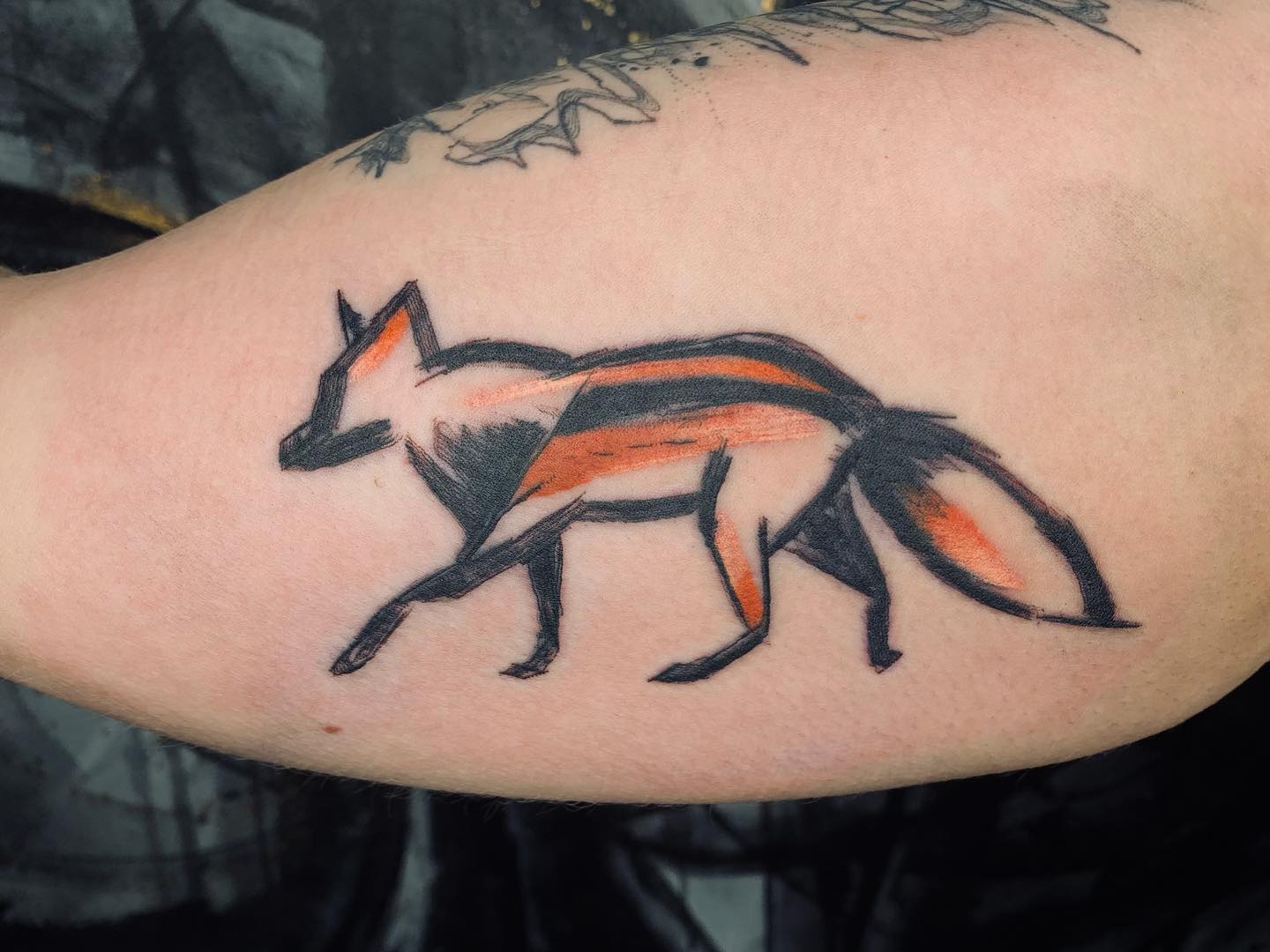 Tatuaje de un zorro pequeño, negro y naranja.