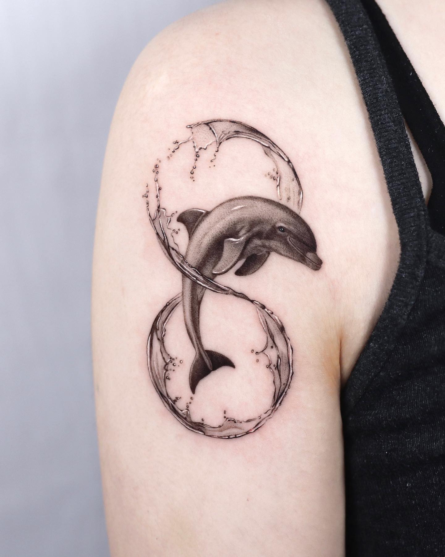 Tatuaje de delfín en el hombro con tinta negra.