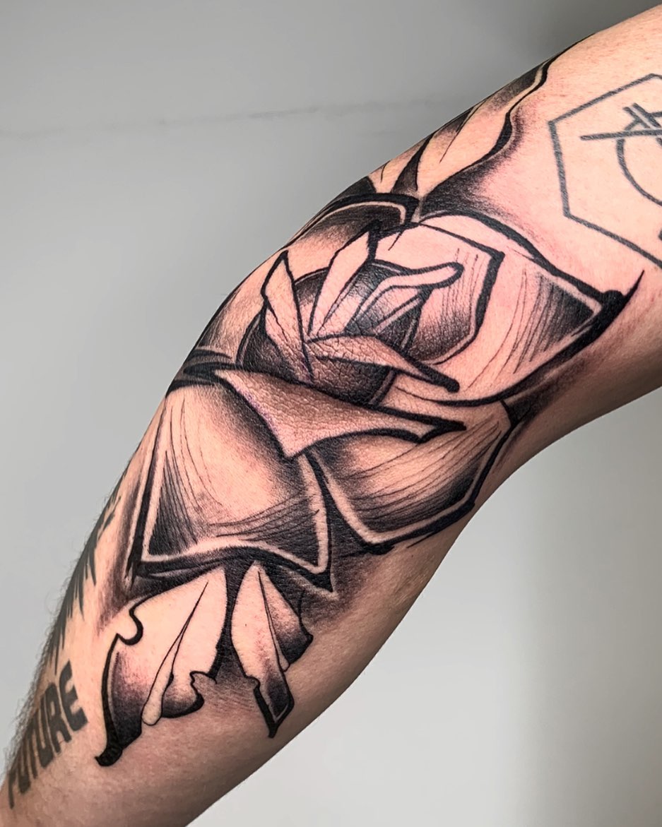 Tatuaje floral de tinta negra en el codo del brazo.