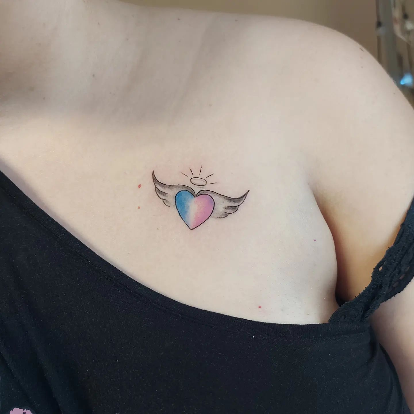 Tatuaje pequeño y colorido de un corazón en la clavícula.