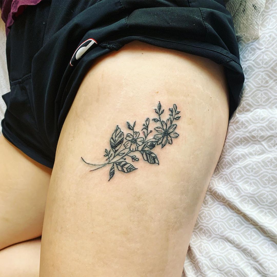 Tatuajes minimalistas de flores en el muslo.