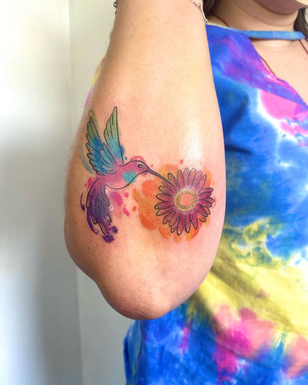 Tatuaje de colibrí colorido rojo en el brazo.