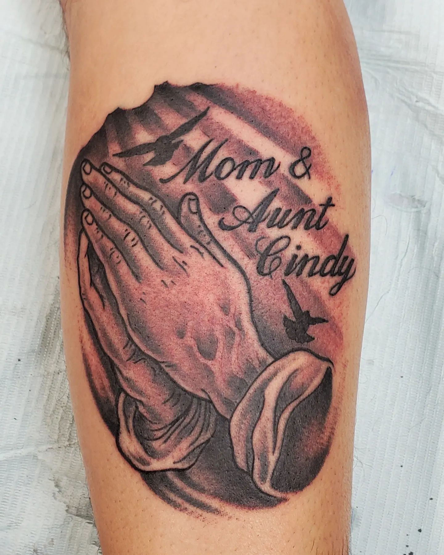Tatuaje de manos rezando con nombres.