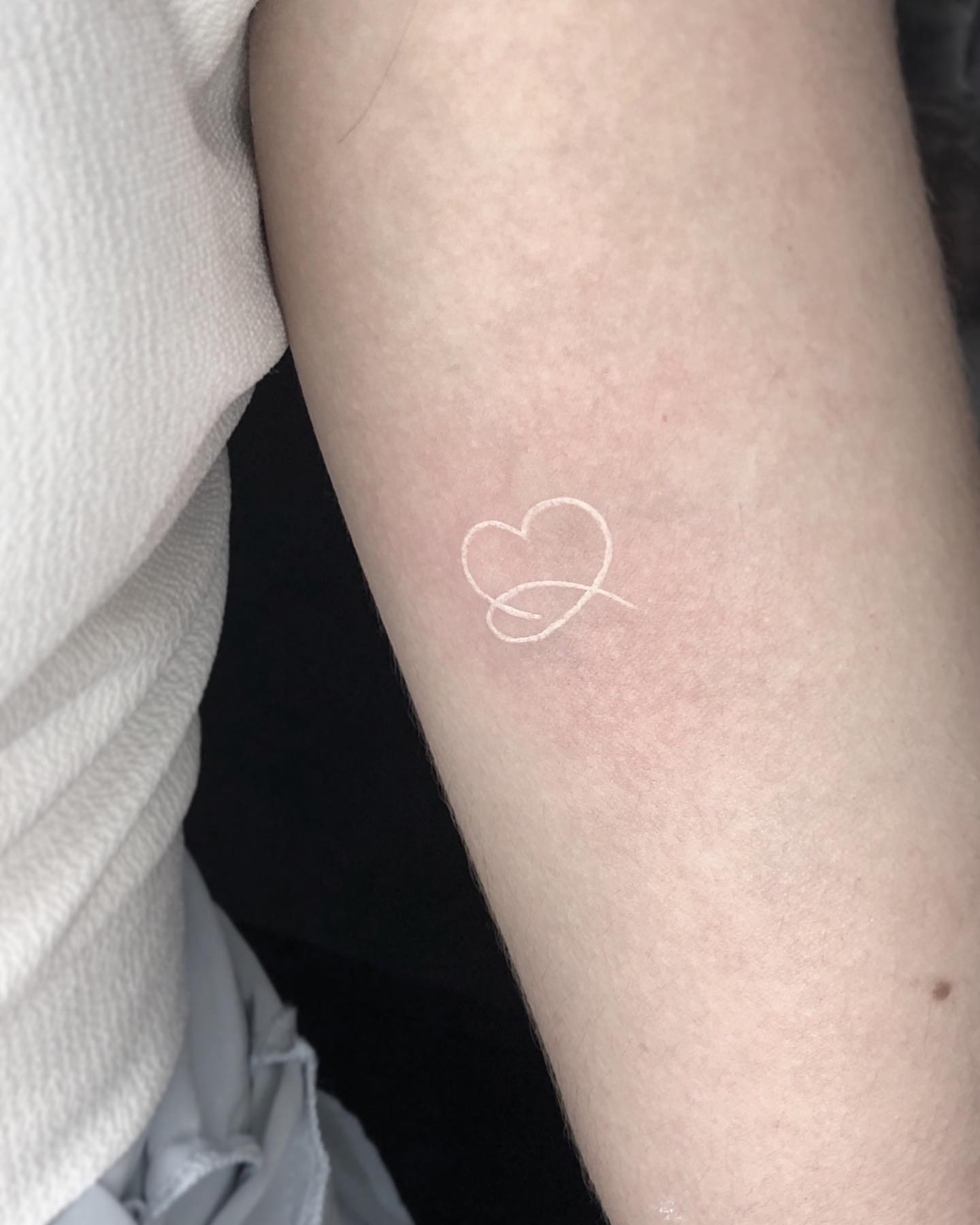 Tatuaje de corazón minimalista con tinta blanca.