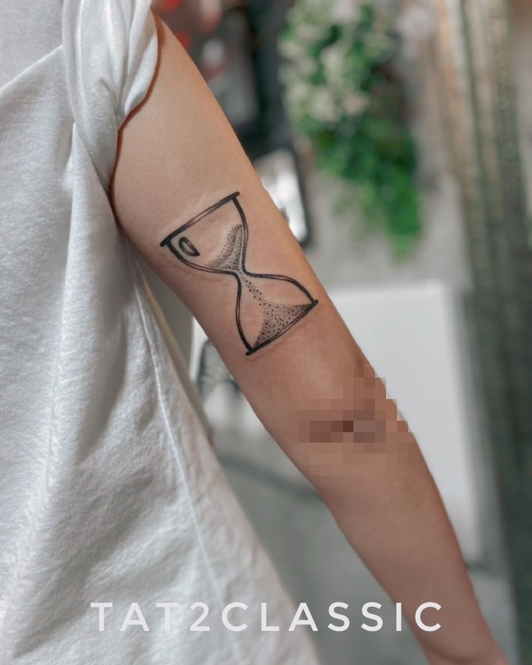 Tatuaje de reloj de arena en tinta negra en el brazo